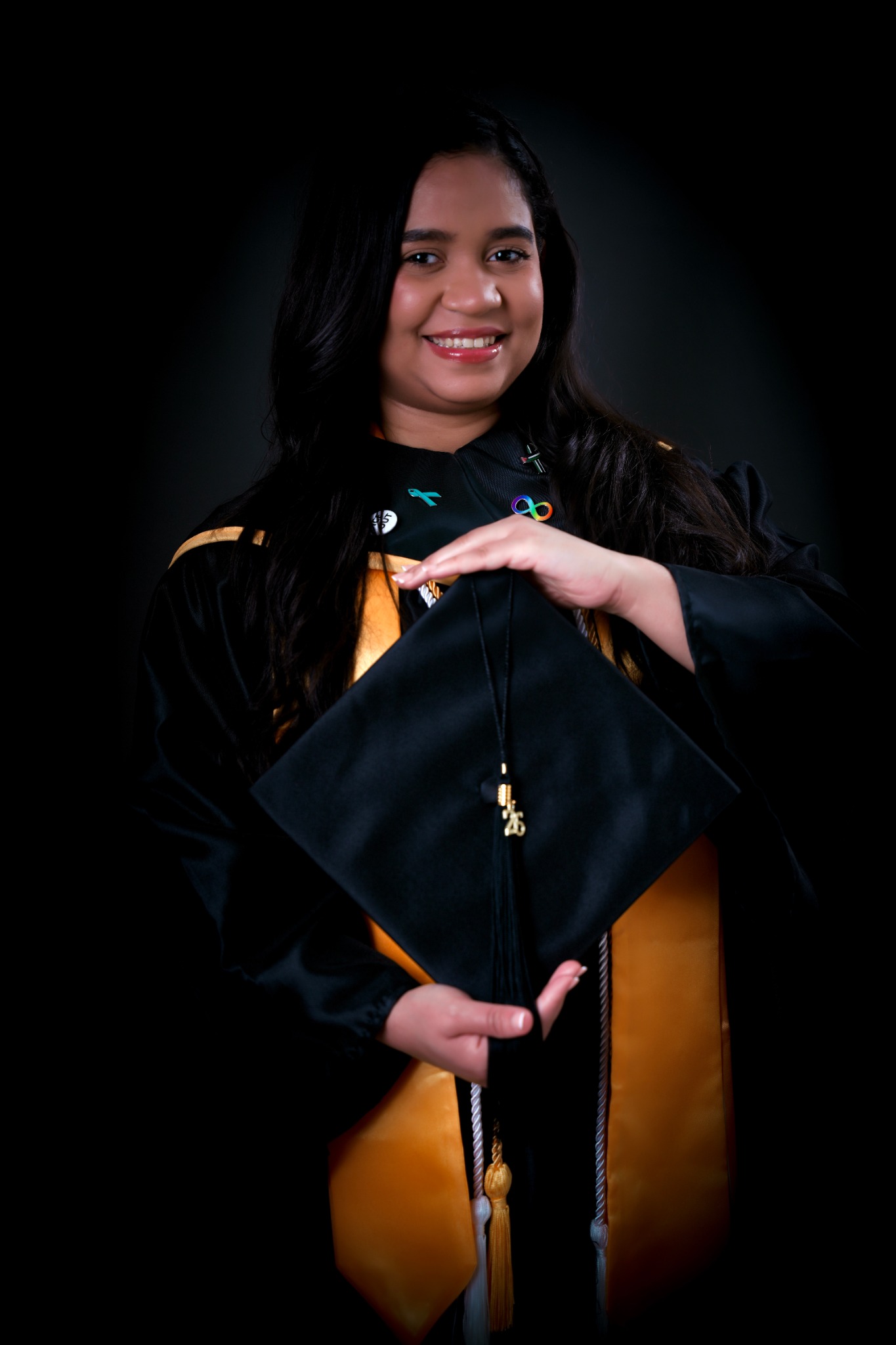 Retrato de graduación en estudio con fondo negro y birrete en las manos